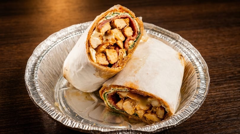Two chicken wraps, cut in half, revealing chicken, cheese, and vegetables, in a foil container.